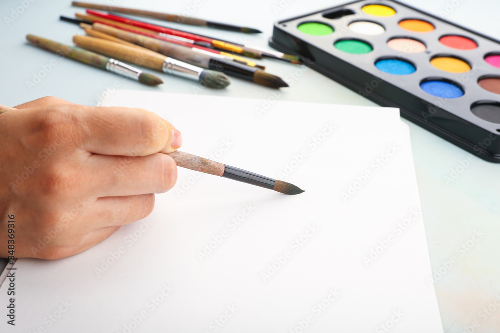 artist’s hand draws with a brush on the background of watercolor paints