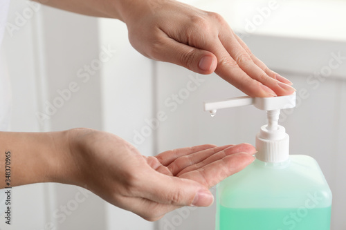 Woman applying antiseptic gel on hand indoors  closeup