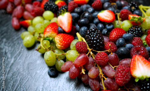 Fototapeta Naklejka Na Ścianę i Meble -  Summer berries food background full frame close up with strawberries, blackberries, blueberries, red, dark and green grapes on black marble.