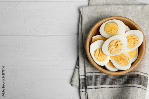 Cut hard boiled chicken eggs in bowl on white wooden table, flat lay. Space for text