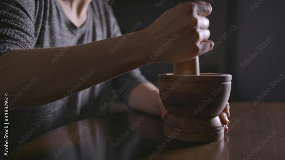 Close up of woman's hands using a mortar and pestle in a dimly-lit room