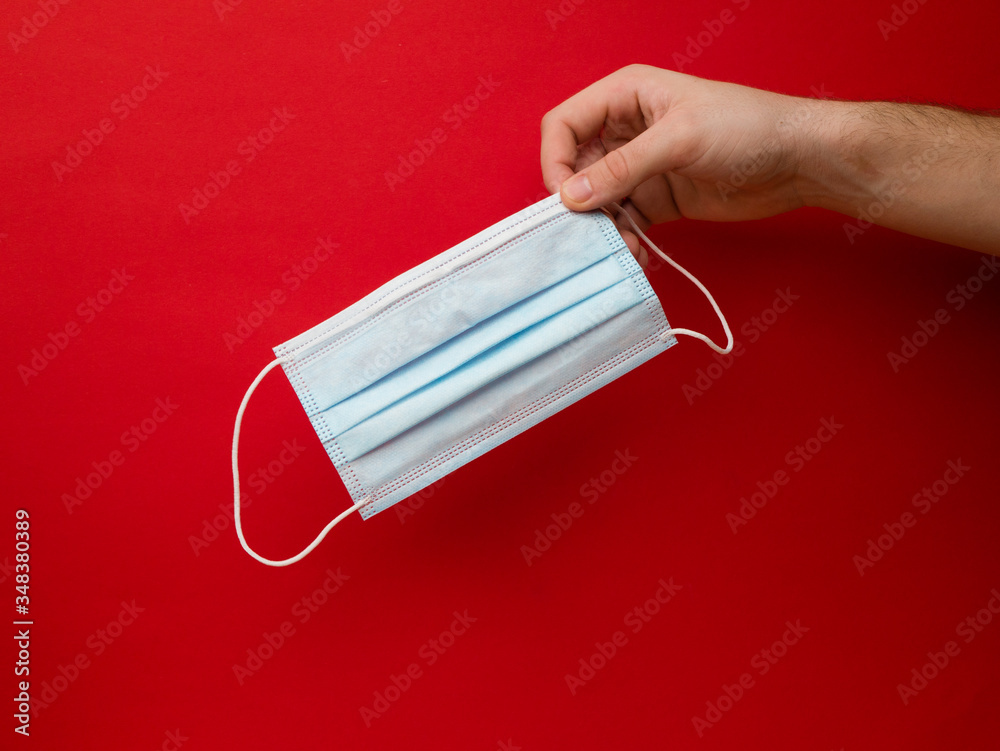 Protective mask in the hand on red background. A young man holds a medical face mask in her hand. Health care concept. Protective mask in the hand on red background. A young man holds a medical face mask in her hand. Health care concept.