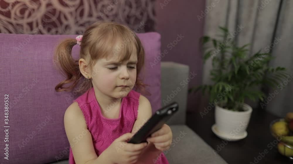 Little child sitting while watching TV. Happy kid girl watch funny music movie Little child sitting while watching TV. Happy kid girl watch funny music movie