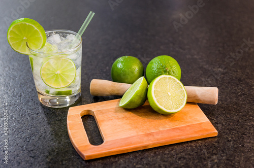 Caipirinha, traditional Brazilian alcoholic drink, typical drink made with sugar, lemon, distilled cane (cachaca) and ice. Ingredients and the drink on black granite surface.
