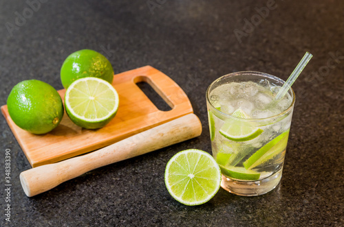 Caipirinha, traditional Brazilian alcoholic drink, typical drink made with sugar, lemon, distilled cane (cachaca) and ice. Ingredients and the drink on black granite surface.