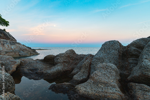 Full moon at spectacular sunset over rocks and sea 