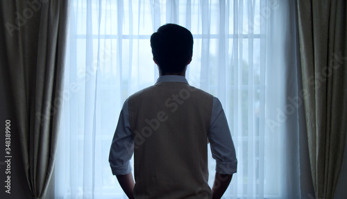Back view of confident young thinking businessman standing before bright window indoors