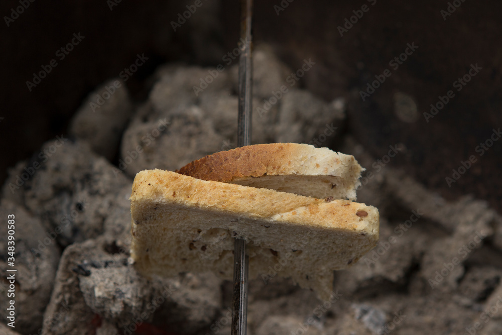 on the brazier, on the fire, almost extinguished with coals, slices of bread is fried on a skewer. A picnic in a forest, park or backyard. on the brazier, on the fire, almost extinguished with coals, slices of bread is fried on a skewer. A picnic in a forest, park or backyard.