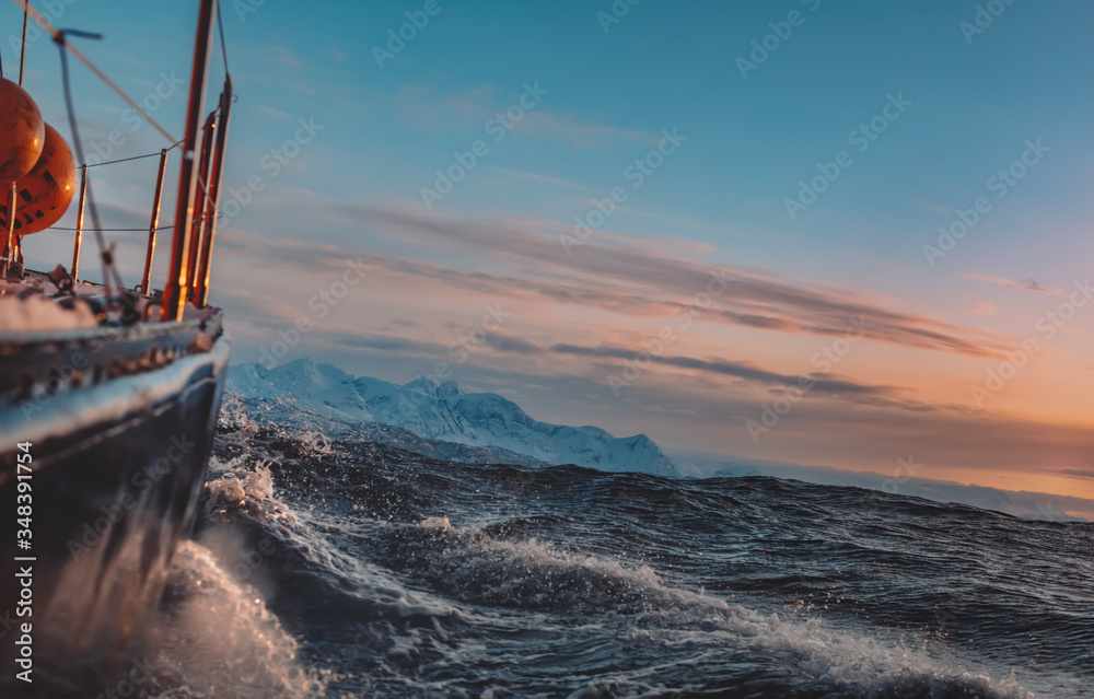 Fototapeta premium Sail boat on rough morning in Norway sea water with splashes, side view with snowy mountains on background