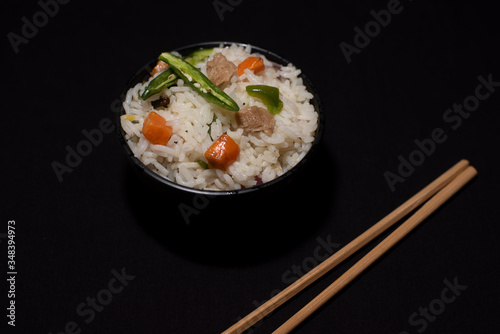 A bowl of rice with vegetables and soya chunks along with chopsticks in a black copy space background. Food photography.