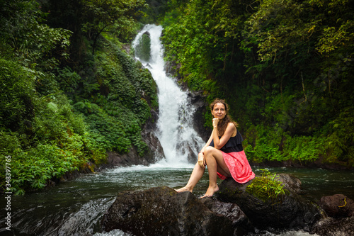 Young Caucasian woman sitting on the rock and enjoiyng waterfall landscape. Travel concept. Dedari waterfall in Sambangan  Bali.