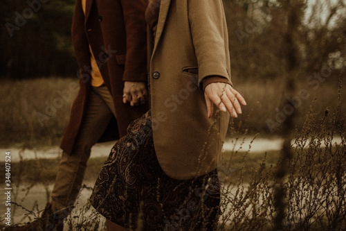 Couple in autumn clothes walks in the field. Hand touching dry grass.