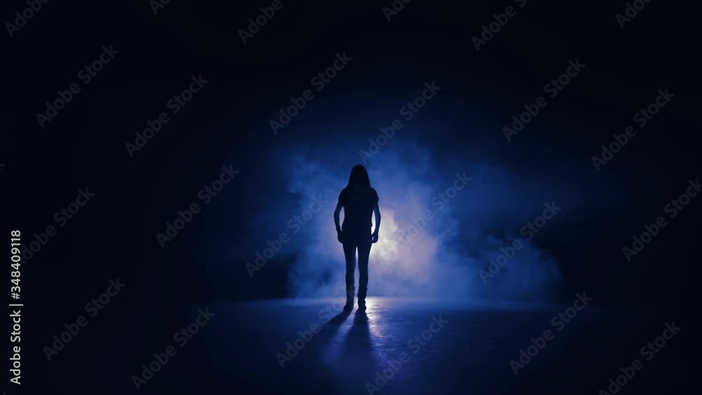 Silhouette of a woman jumping in front of a blue light.Wide shot of a female dancer performing in front of a light in a studio. Silhouette of a woman jumping in front of a blue light.Wide shot of a female dancer performing in front of a light in a studio.