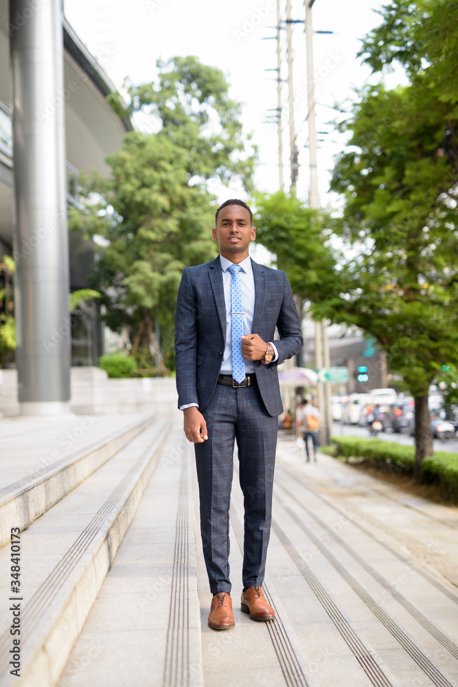 Full body shot of happy young African businessman smiling in the city streets outdoors Full body shot of happy young African businessman smiling in the city streets outdoors