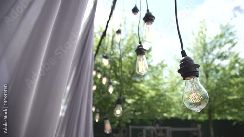 4K video light bulb Edison wired vintage style is hanging during event in nature cinematic shot in slow motion in focus and out of focus stylish wedding event ceremony outdoors event 