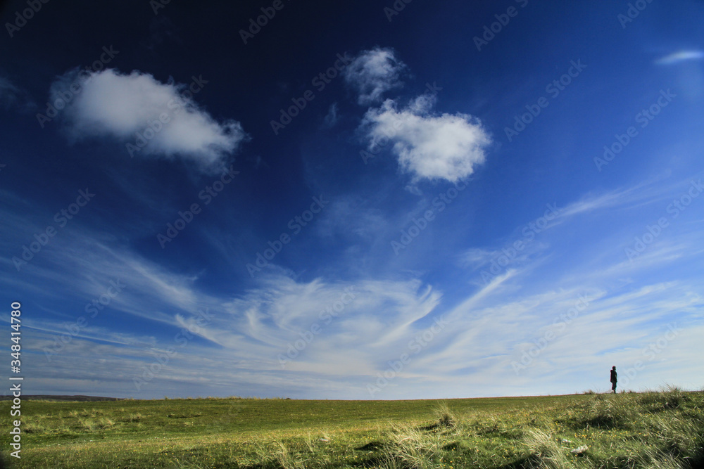 Wolkenwirbel hoch am Himmel und einsamer Spaziergänger am Horizont