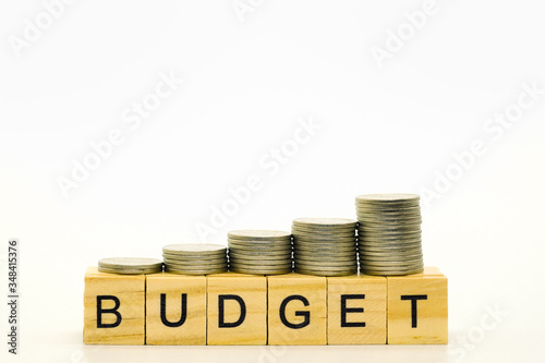 Closeup of stack of silver coins on top of wooden block word budget and white background with copy space for text.