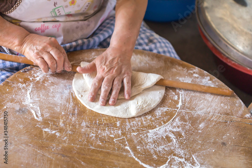 Woman in a black chef's apron roll out the dough for preparing Turkish pancake. Woman rolls out dough, close-up. Making Turkish traditional flat cakes.