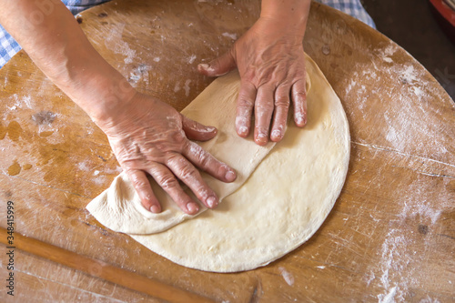 Woman in a black chef's apron roll out the dough for preparing Turkish pancake. 
Woman rolls out dough, close-up. Making Turkish traditional flat cakes.