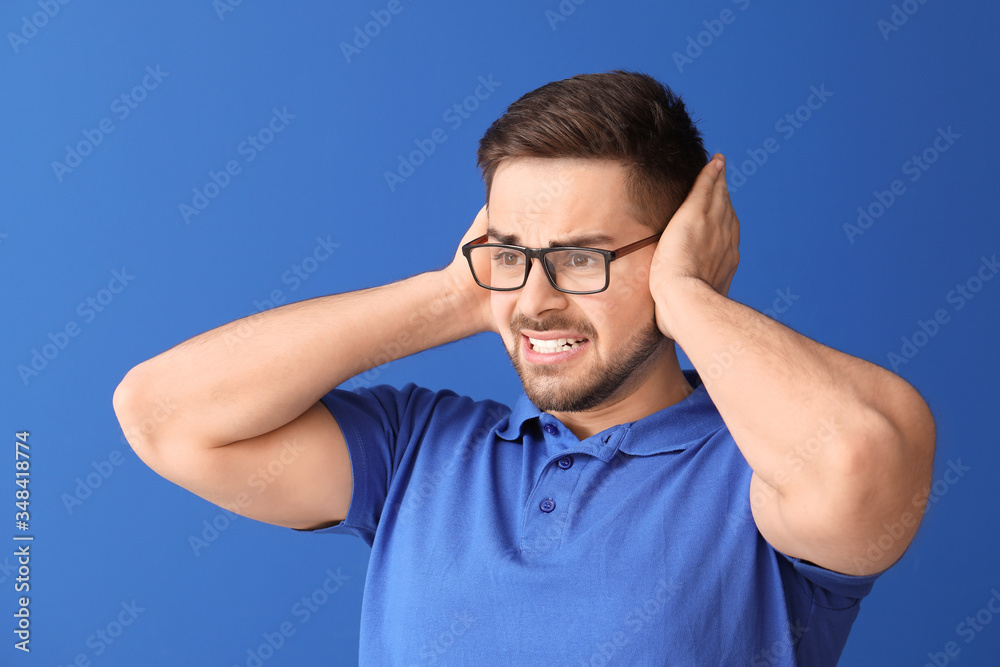 Young man suffering from loud noise on color background Young man suffering from loud noise on color background
