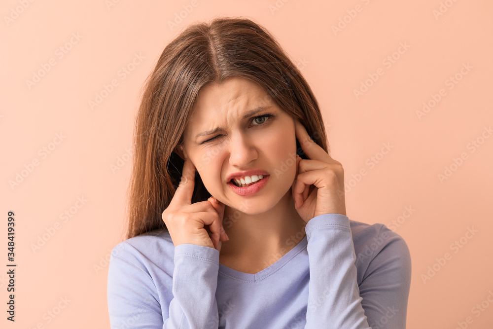 Young woman suffering from loud noise on color background Young woman suffering from loud noise on color background