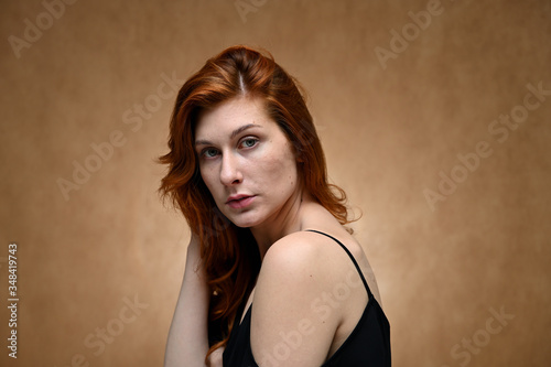 Studio large photo portrait of a caucasian young woman with long red hair on a beige background.