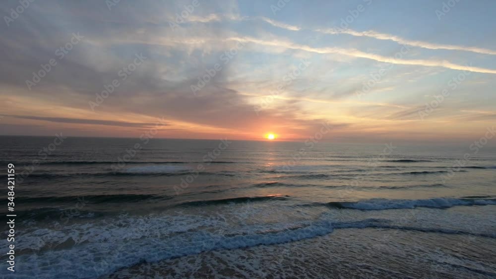 Aerial view of ocean waves crashing with bright colorful sunrise in the distance. Aerial view of ocean waves crashing with bright colorful sunrise in the distance.