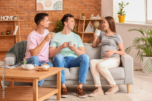 Gay couple with pregnant woman drinking tea at home photo