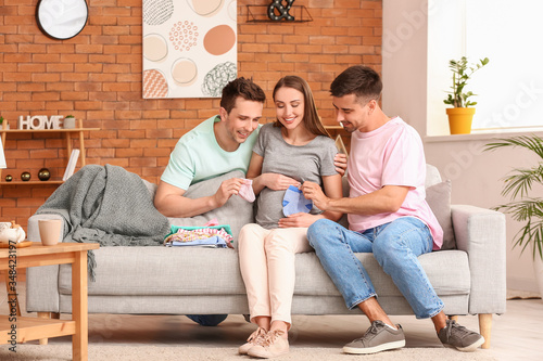 Gay couple and pregnant woman with baby clothes at home photo