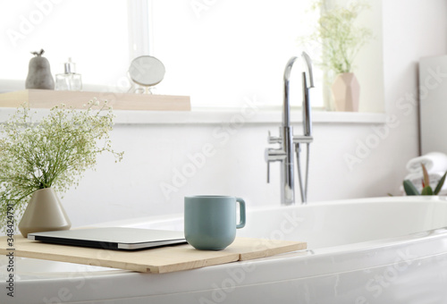 Stand with floral decor  laptop and cup of coffee on bathtub