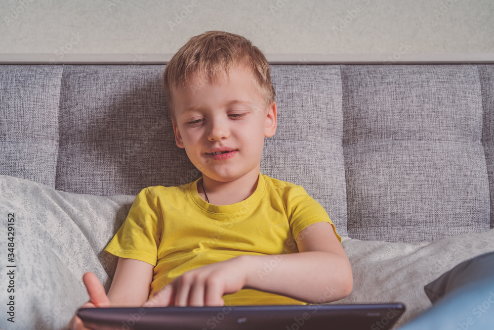 Distance education, learning. Boy is sitting on the bed with a tablet in the room. Child with a gadget. Teenage child using tablet pc. Distance education, learning. Boy is sitting on the bed with a tablet in the room. Child with a gadget. Teenage child using tablet pc.