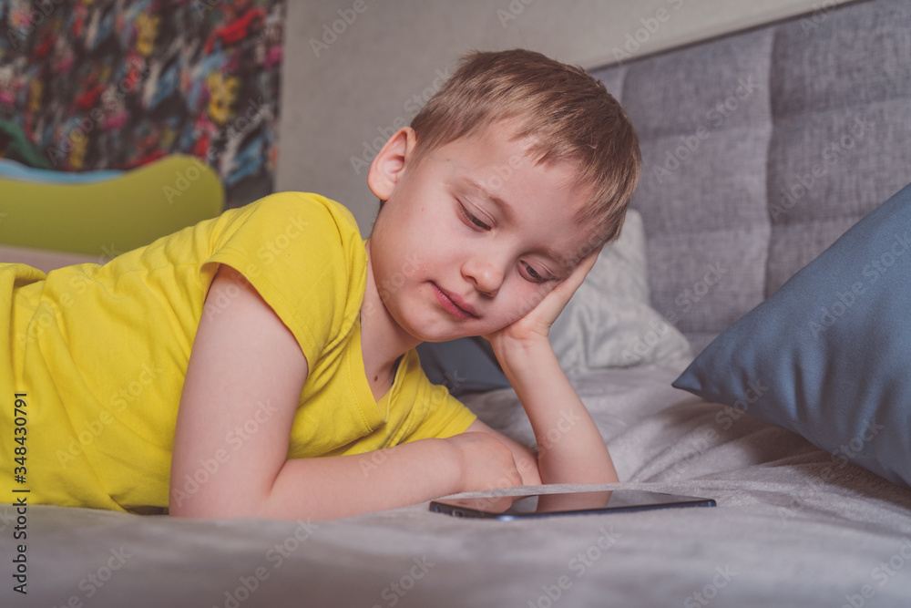 Distance education, learning. Boy is lying on the bed with a smartphone in the room. Child with a gadget. Teenage child using smartphone.