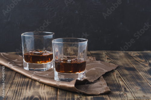 Two Glasses of whiskey with ice cubes on a wooden table/Two Glasses of whiskey with ice cubes on a wooden table. Black background with copyspace.