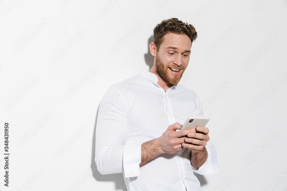 Image of handsome joyful man in shirt typing on cellphone and smiling Image of handsome joyful man in shirt typing on cellphone and smiling