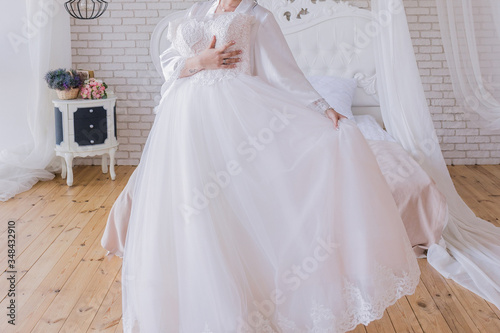 the bride in a peignoir holds a wedding dress