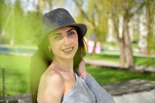 Model posing in spring park outdoors with a smile. Close-up portrait of a cute young caucasian brunette girl in a gray dress and black hat in various poses.
