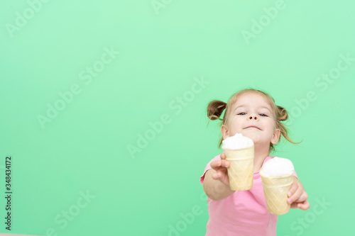 little girl 4 years old in a pink T-shirt on a green background holds ice cream in his hands and holds out two ice-cream to the viewer, mock-up with place for text