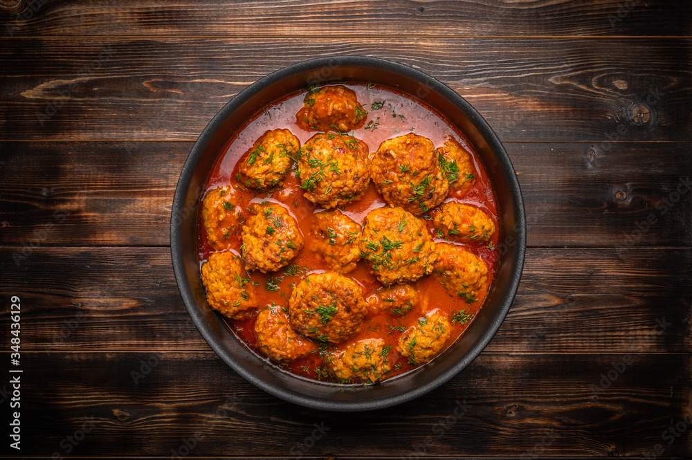 Homemade meatballs in tomato sauce with herbs in a saucepan on a dark wooden background. Top view