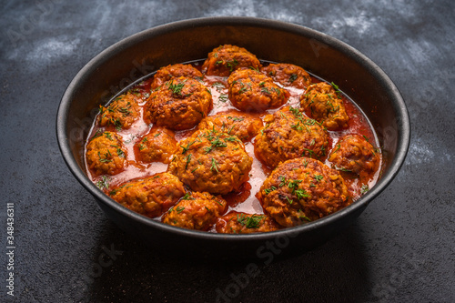 Homemade meatballs in tomato sauce with herbs in a saucepan on a dark wooden background