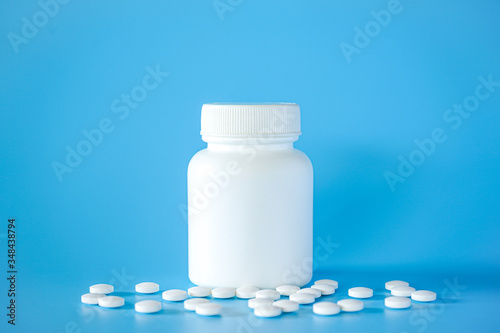 White plastic pill bottle with teblets pills on blue background with selective focus photo