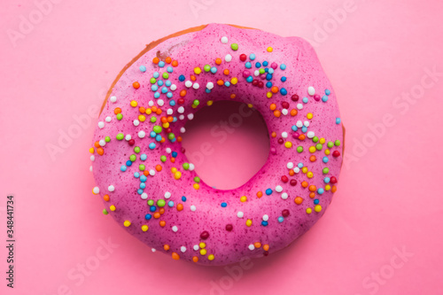 Homemade circle donut with pink icing and rainbow sprinkles on the trendy soft pink background situated on center. Free copy space. Doughnut pastry.