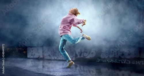 Female street dancer in a action with a graffity wall behind the fog on a backgroung. photo