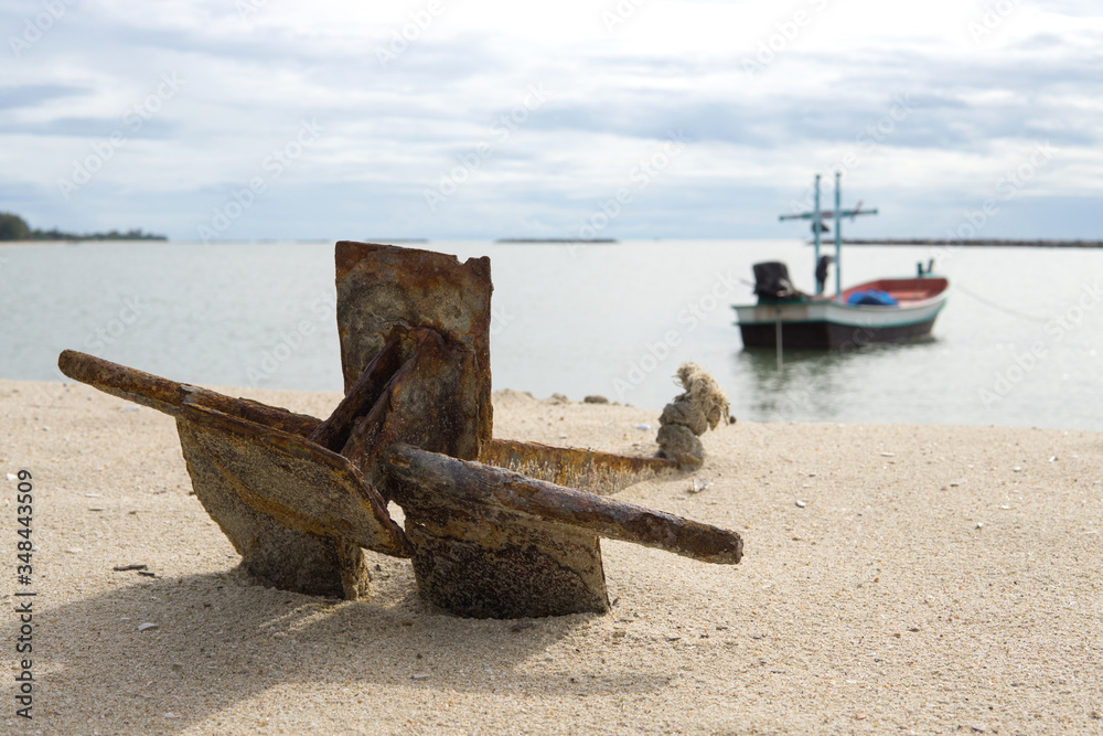 Close up of old Anchor on the beach. Small wooden fishing boat anchored on the beach.