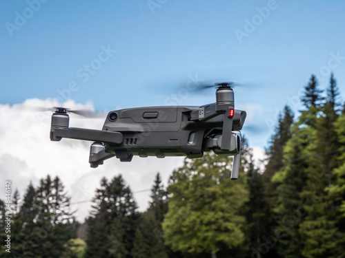 A drone is captured in a stationary hover in front of the camera. The drone is hovering in forest nature area in Switzerland.