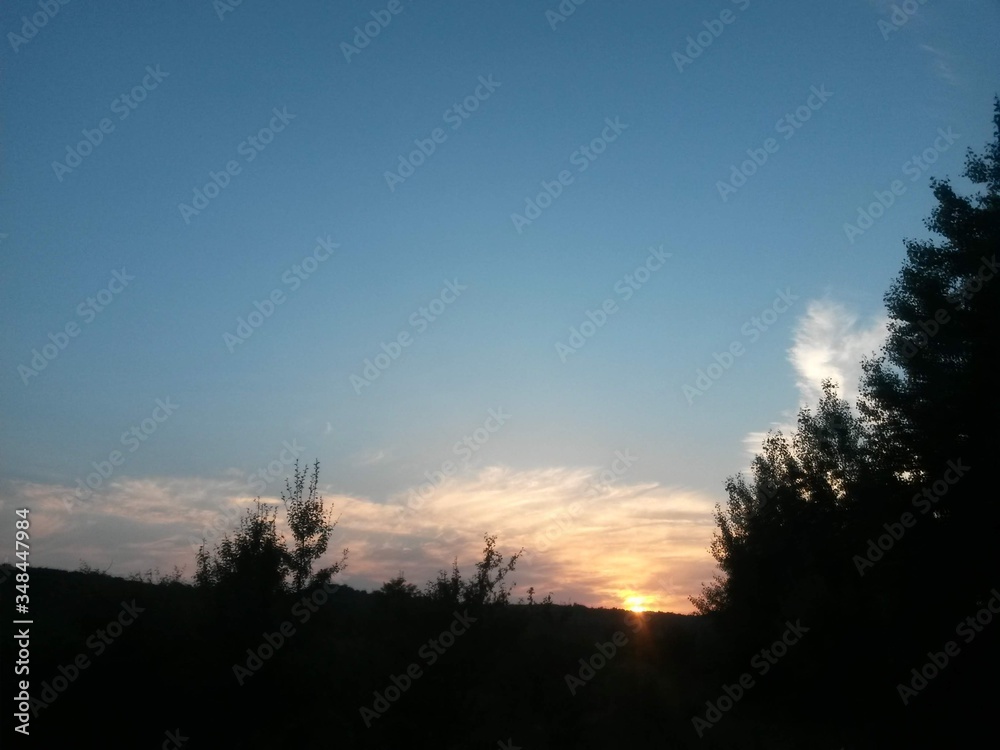 Obraz premium sunset coloring the clouds among the trees