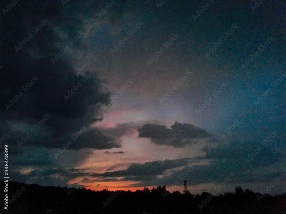 Fototapeta premium sunset coloring the clouds among the trees