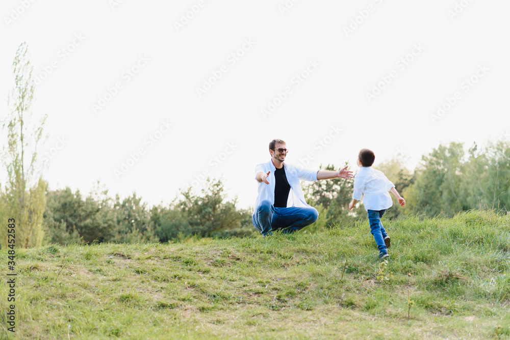 Handsome dad with his little cute son are having fun and playing on green grassy lawn. Happy family concept. Beauty nature scene with family outdoor lifestyle. family resting together. Fathers day