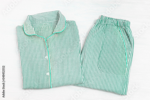 Folded pajama with striped neo-mint color on white wooden surface with copy space. Night suit for sleeping. Top view. Flat lay.
