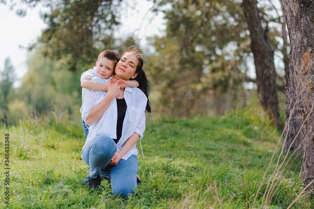 Fototapeta premium Happy young mother is playing with her baby in a park on a green lawn. Happiness and harmony of family life. Great family vacation. Good weekend. Mothers Day. Holiday. The concept of a happy family