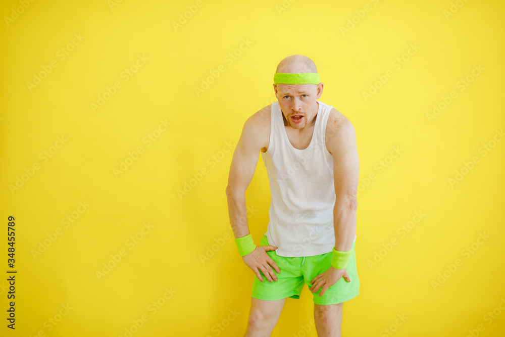 Tired after training, funny bald man in a sports uniform on a yellow background in a confident pose looks at the camera. retro style